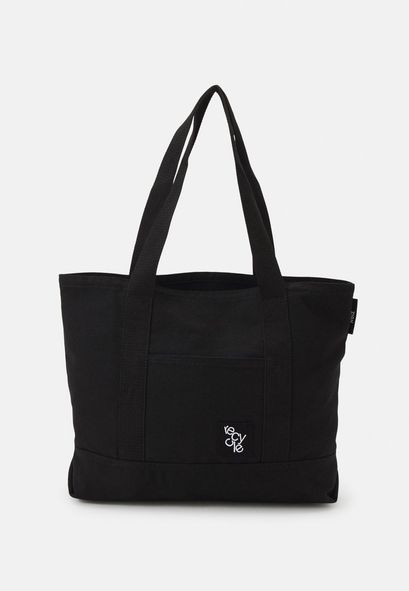 Sac cabas noir avec longues anses, poche avant et petit patch "recycle" sur la poche, sur un fond uni.