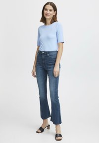 Top azzurro chiaro aderente a maniche corte, jeans scuri a zampa d'elefante con orli sfrangiati, sandali neri con tacco, design semplice, texture liscia.