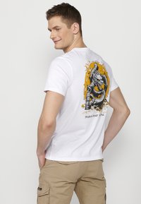 White cotton T-shirt featuring an intricate dragon graphic in black and vibrant orange, with water splashes and text on the back.
