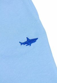 Lichtblauwe T-shirt met een geborduurd ontwerp van een blauwe haai. Zachte stof met een gladde textuur en korte mouwen.