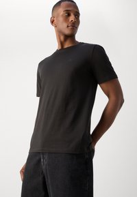 Sort bomulds t-shirt med rund halsudskæring, korte ærmer og slim fit. Har et subtilt logo på brystet og en glat tekstur.