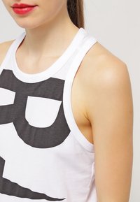 Vit linne med en stor svart grafisk design framtill, med rund halsringning och racerback. Mjuk tyg och figurnära passform.