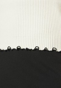 Vit ribbad tyg med svarta vågiga kanter på toppen av slät svart tyg.