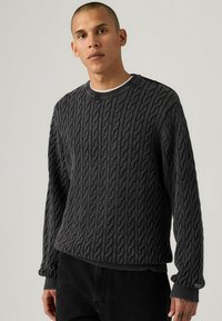 Grey cable-knit sweater with a round neckline and ribbed cuffs. Features a textured pattern and is made from a soft, thick material.