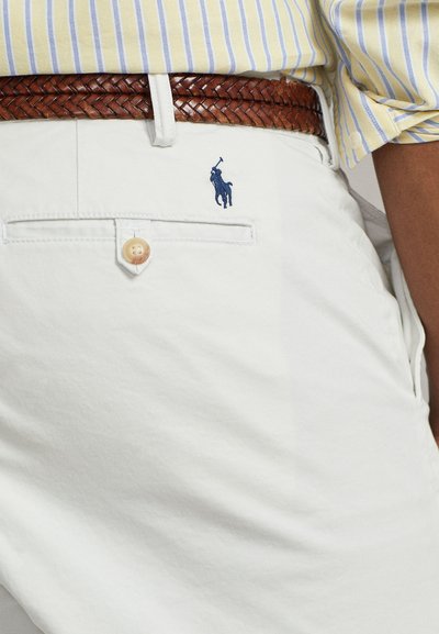 Λευκά σορτς από βαμβάκι με έναν πλεγμένο καφέ δερμάτινο ζώνη. Διαθέτει μία πίσω τσέπη με μπλε κεντητό λογότυπο αλόγου και κουμπί.