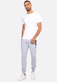 Weißes T-Shirt mit Rundhalsausschnitt, kombiniert mit hellgrauen Jogginghosen mit Seitentaschen und einem schwarzen Akzentlogo, ergänzt durch weiße Sneaker.