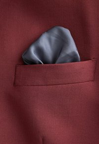 Burgundi színű öltönyszövet texturált felülettel; egy szürke zsebkendő kandikál ki egy egyenes zsebből.