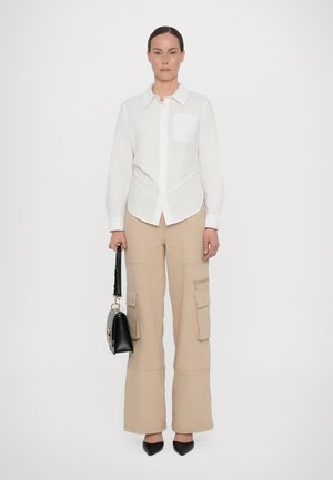 Camicia bianca a maniche lunghe con tasca, abbinata a pantaloni cargo beige a gamba larga con tasche laterali e dettagli cuciti. Borsa nera e tacchi a punta.