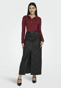 Zwarte denim maxi rok met een split aan de voorkant, gecombineerd met een aansluitend bordeauxrood longsleeve polo-shirt met een knoopsluiting.