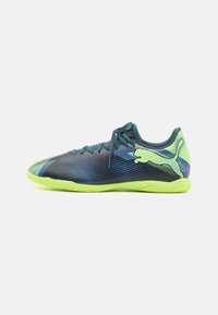 Zapatillas deportivas con un diseño aerodinámico, que presentan una parte superior negra con acentos en azul y verde, y una suela exterior verde brillante para mayor tracción.
