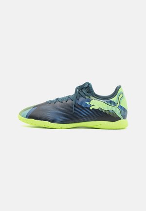 Zapatillas deportivas con un diseño aerodinámico, que presentan una parte superior negra con acentos en azul y verde, y una suela exterior verde brillante para mayor tracción.