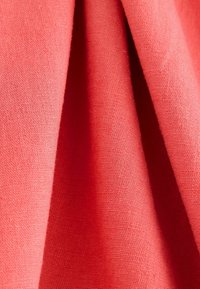 Tessuto color corallo con una finitura testurizzata, caratterizzato da morbide e fini trame e sottili variazioni di tonalità e tonalità.