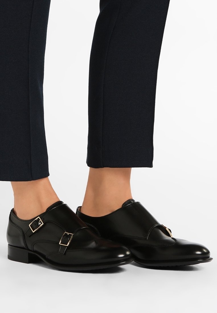 Chaussures habillées en cuir noir à double bride monk portées avec un pantalon slim foncé sur fond blanc.