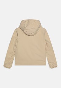 Beige hettejakke med en glatt, matt tekstur. Har et strømlinjeformet design og elastiske mansjetter, som gir en tettsittende silhuett. Bakvisning.