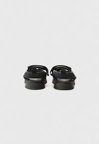Black sandals with a thick rubber sole, featuring adjustable elastic straps and a smooth finish on the upper section.