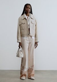 Bēšs īss žakete ar lielām kabatām, valkāts virs balta krekla. Mīkstas rozā bikses ar ziedu rakstiem, kopā ar mazu baltu somiņu.