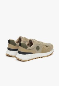 Beżowe sneakersy z górą wykonaną z tekstyliów i zamszu, zielonymi akcentami, białą podeszwą środkową oraz teksturowaną brązową podeszwą. Posiadają wyściełany kołnierz i system sznurowania.