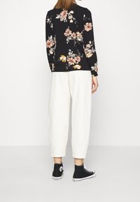Langärmliges schwarzes Oberteil mit floralen Mustern in Rosa und Gelb, kombiniert mit lockeren cremefarbenen Hosen und schwarzen High-Top-Sneakern.