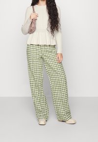 Béžový pletený top s dlouhým rukávem a peplum lemem ve spodní části, doplněný zeleno-bílými širokými kalhotami s kašmírovým vzorem. Krémové nazouvací boty.