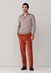 Lichtgrijze zip-up trui, oranje corduroy broek en bruine schoenen. De trui heeft een gestructureerde afwerking; de broek heeft verticale ribbels.