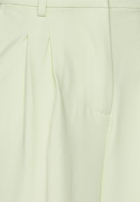 Lichtgroene op maat gemaakte broeken met voorplooien, een soepele textuur en een zijzakdetail. Gemaakt van een zachte, lichte stof.