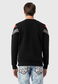 Zwarte sweatshirt met rode, grijze en zwarte accenten op de schouders; heeft een simpele ronde hals en ribgebreide manchetten. Gekocht met lichtdenim jeans met geborduurde details.