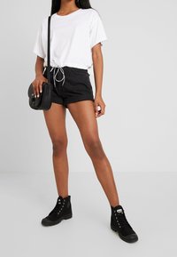 Camiseta corta blanca con dobladillo con cordón, combinada con pantalones cortos de mezclilla negros y botas negras hasta el tobillo. Diseño sencillo, esquema de color minimalista.
