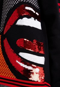 Röda och vita paljetterade läppdesign på en svart tygbakgrund med mönster i grå och orange nyanser.