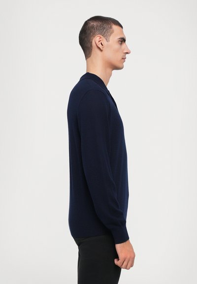 Pulover navy cu mâneci lungi și guler polo. Textură moale, siluetă ajustată și mansete cu striații. Purtați peste pantaloni negri slim-fit.