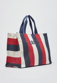 Sac fourre-tout rayé en rouge, blanc et marine, en tissu texturé. Comprend deux poignées solides et un détail de logo sur le devant.