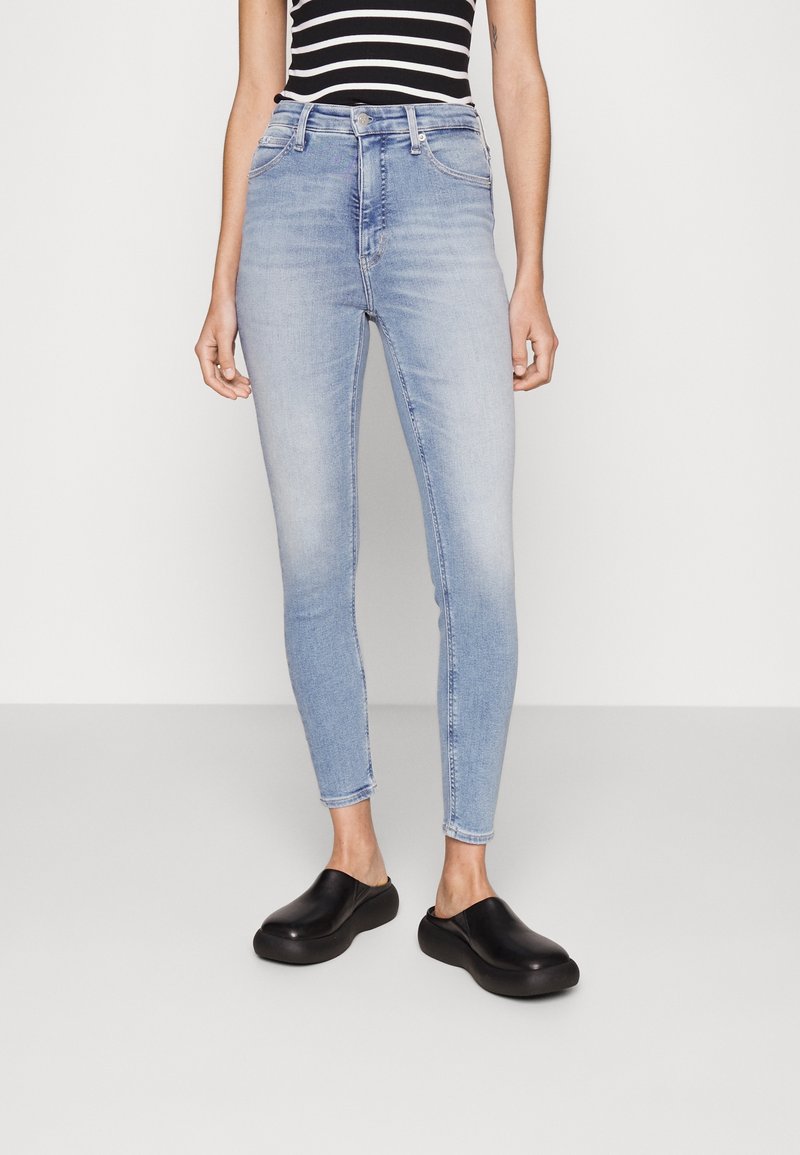 Jeans ajustados de tiro alto en azul claro con una textura de denim suave. Combinados con una blusa de rayas en blanco y negro y zapatos negros de tipo slip-on.