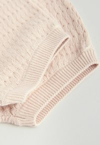 Tissu tricoté rose clair avec un motif torsadé et des bords côtelés, plié sur une surface claire.