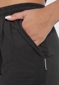 Pantaloni jogger neri con un tessuto morbido e testurizzato, dotati di una tasca laterale e di un'etichetta del marchio visibile. La vita è elasticizzata per un fit confortevole.