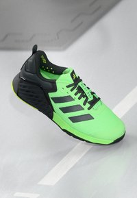 Baskets de sport vertes avec une tige en maille texturée, des accents noirs et trois rayures noires. Semelle entièrement noire avec un talon rembourré.
