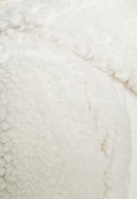 Bílá, měkká umělá kožešina s texturovaným, hebkým povrchem. Obsahuje zaoblené tvary a jemné křivky ve svém designu.