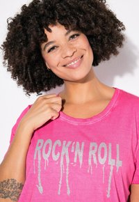 Růžové tričko s krátkým rukávem vyrobené z bavlny, s kovovým stříbrným potiskem "ROCK'N ROLL" s kapajícím efektem. Kolo výstřih a volný střih.