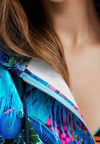 Kolorowa bluza z kapturem na zamek, zdobiona kwiatowym i abstrakcyjnym wzorem w odcieniach niebieskiego, różowego i zielonego. Miękka tkanina z kontrastową podszewką wewnętrzną.