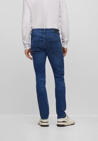Slim blå jeans av denim med midjEHöjd och två bakfickor. Matchas med vita sneakers och en ljus skjorta.