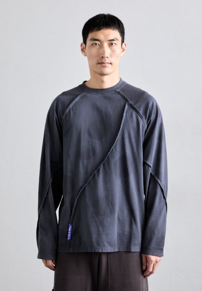 Camisa gris de manga larga hecha de algodón con un diseño de costura diagonal texturizada y etiqueta de logo, presenta un cuello redondo y un ajuste relajado.