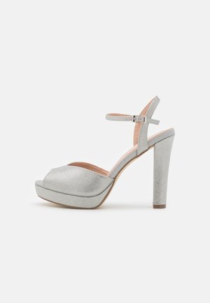 Talons hauts en plateforme argentée avec une finition texturée, orteils ouverts et bride de cheville. Le design à talon épais offre stabilité et soutien.