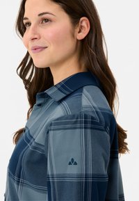 Camicia a quadri blu con accenti blu scuro, design con bottoni frontali e colletto. Presenta un tessuto testurizzato e un piccolo logo sulla manica.