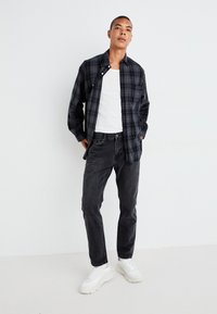 Zwart en marineblauw geblokt overhemd over een witte tanktop, gecombineerd met zwarte jeans en witte sneakers. Hedendaagse pasvorm, casual ontwerp.