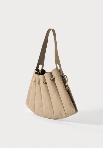 Krémová nubuková kabelka s plisovaným designem, jedním širokým ramenním popruhem a zlatým zapínáním na korálky na bílém pozadí.