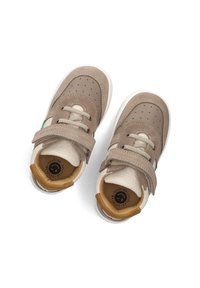Beige Sneakers in Kindergröße mit durchlöchertem Zehenbereich, Klettverschluss, Schnürsenkeln und gepolstertem Kragen, von oben auf weißem Hintergrund betrachtet.