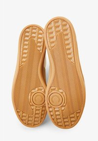 Suelas de zapatos con un material de goma texturizado, que presentan patrones hexagonales y surcos en zigzag para tracción, en un color marrón claro.