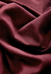 Burgundy fabric with a smooth texture and slight sheen, displaying folds and creases that highlight its soft composition.