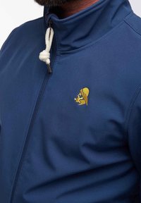 Giacca zip-up blu con collo alto, dotata di un cordino bianco e un logo ricamato giallo di un leone con un cappello. Texture liscia.