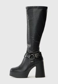 Bottes noires montantes à plateforme avec une finition brillante, dotées d'un large talon bloc et d'une sangle à boucle au niveau de la cheville.