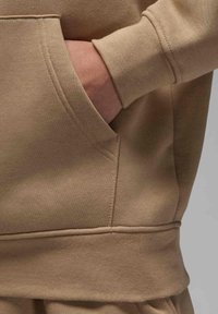 Felpa beige con tasca a marsupio, polsini e orlo a costine. Tessuto morbido con una finitura liscia, che presenta dettagli di cucitura ordinati.