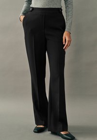 Crne formalne hlače visokog struka, s dva dugmeta sprijeda, bočnim džepovima i elegantnim, krojenim fitom. Uredne nabore sprijeda.